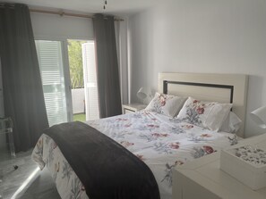 A bedroom with a bed, a nightstand, a lamp, and a view of the outdoors through a sliding door.