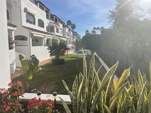 A white building with balconies, a well-maintained lawn, and tropical plants.