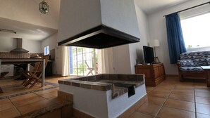 Un vaste espace de vie doté d’une cheminée, d’un ventilateur de plafond et d’une grande fenêtre agrémentée de rideaux.