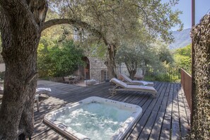 Une terrasse en bois avec un jacuzzi, des chaises longues et un bâtiment en pierre en arrière-plan.