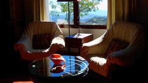 A room with two chairs facing a window with a view of a mountain range. There is a lamp on a small table between the chairs.
