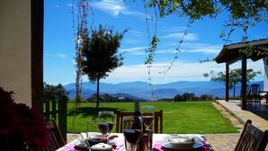 An outdoor dining table set with plates, glasses, and a lantern, overlooking a grassy landscape and mountains.