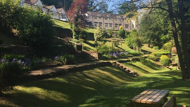 Un jardin bien entretenu, avec une table de pique-nique, une végétation luxuriante et une vue sur une rangée de maisons en arrière-plan.
