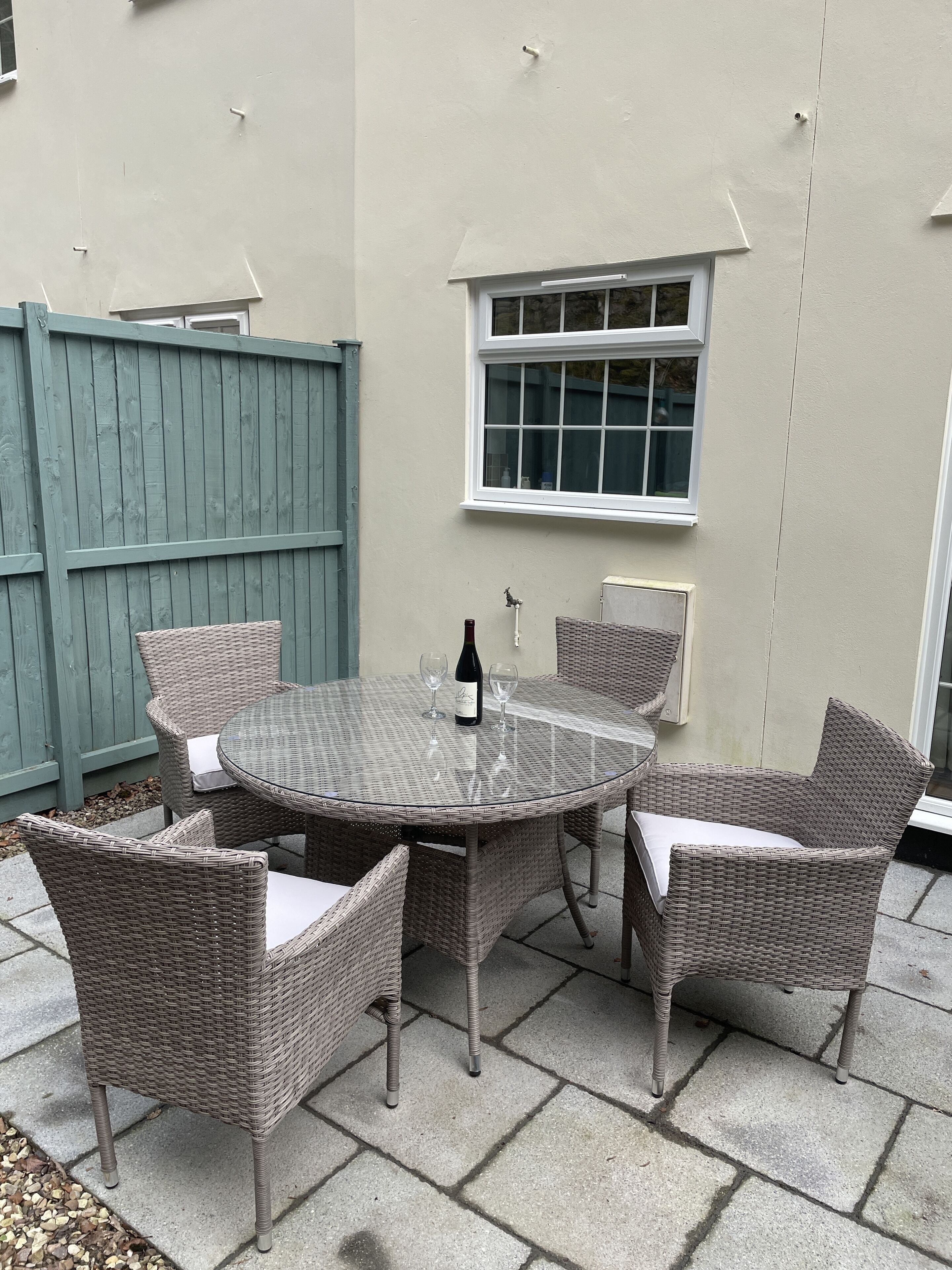 A round glass-top table with wicker chairs, a bottle of wine, and two wine glasses.