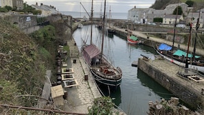 A narrow waterway with boats docked on both sides, stone walls, and buildings in the background. - PRISTINE APARTMENT, 4 MIN WALK TO PRIVATE BEACH, STUNNING SEA VIEWS. (Duporth)