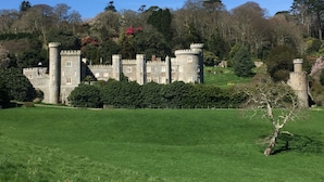 A castle with multiple towers and a well-maintained lawn in the foreground. - PRISTINE APARTMENT, 4 MIN WALK TO PRIVATE BEACH, STUNNING SEA VIEWS. (Duporth)