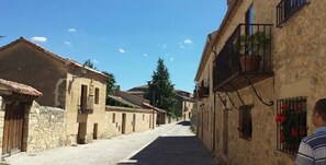 A narrow street lined with traditional stone buildings, some with balconies and potted plants.
