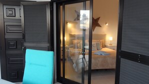 Una moderna camera d'albergo con una porta scorrevole in vetro che dà su un balcone, un letto decorato con una stella e un comodino con una lampada.