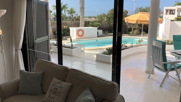 Una stanza con una grande finestra che si affaccia su una zona piscina, un divano con un cuscino e una poltrona.