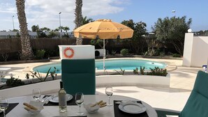 Area pranzo a bordo piscina con un tavolo per due, un salvagente e un ombrellone giallo.