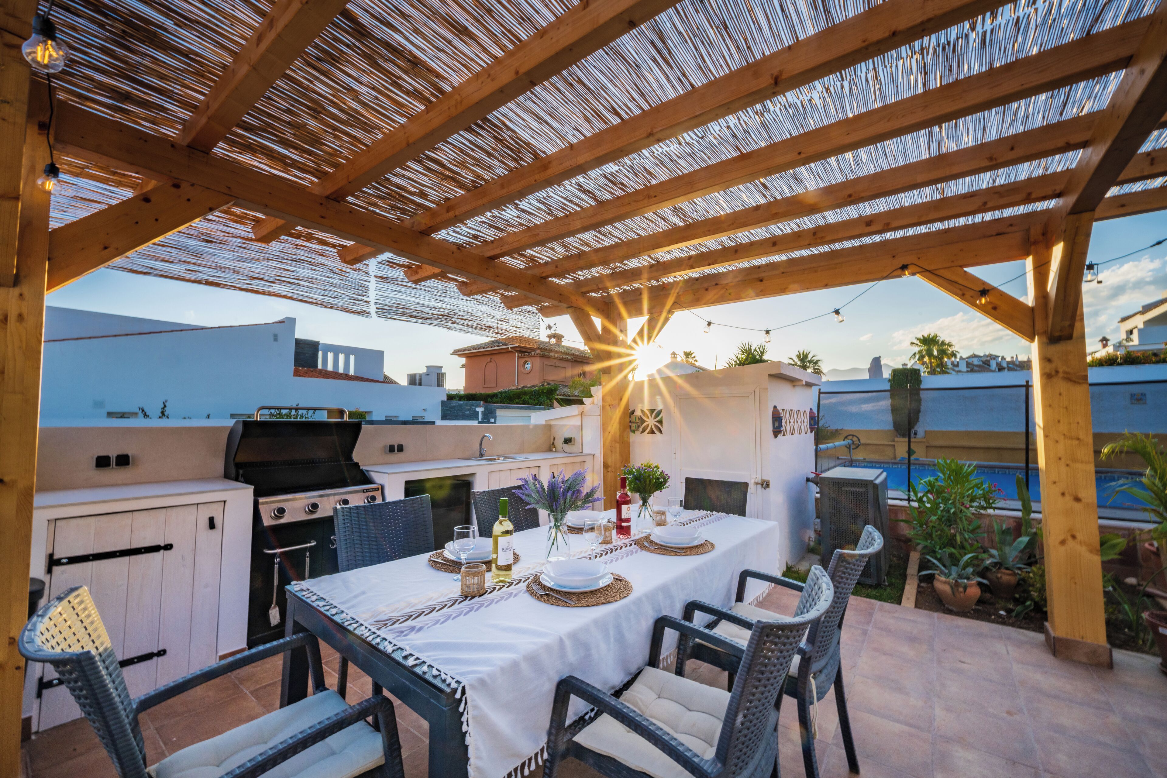 Um pátio externo com uma mesa de jantar posta para quatro pessoas, cercado por cadeiras de vime.