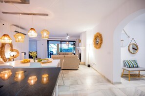 Et moderne køkken med en central ø, hængende lamper og et spiseområde med en bænk.