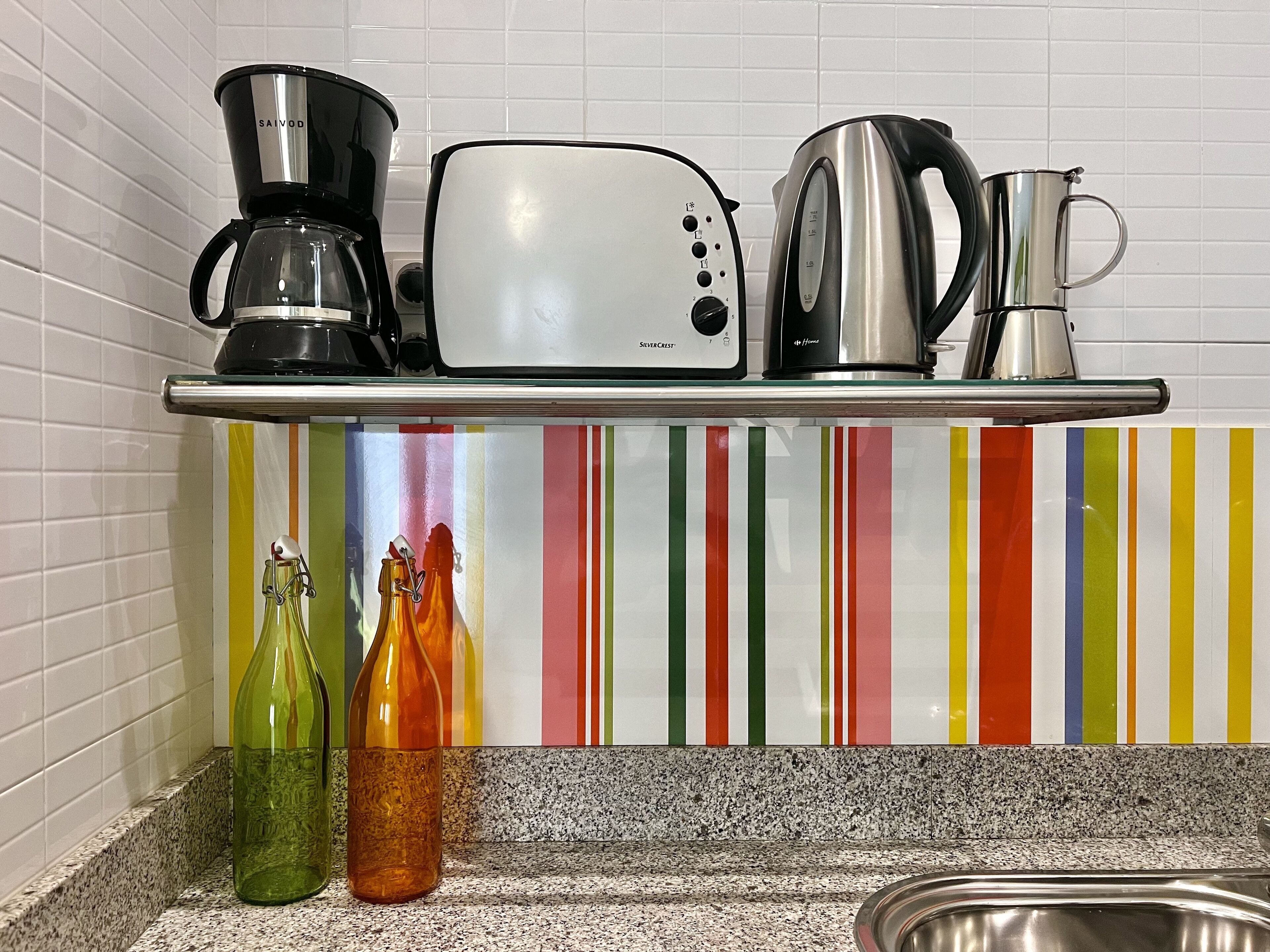 A kitchen counter with a coffee maker, toaster, kettle, and two bottles.