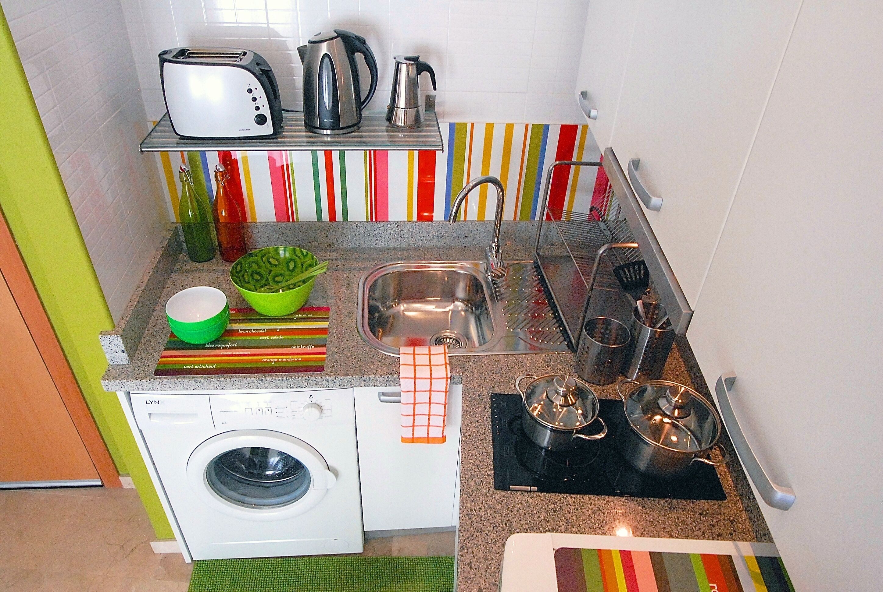 Eine kompakte Küche mit Waschmaschine, Toaster, Wasserkocher und Spüle.
