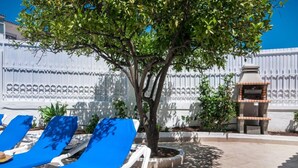 A patio area with blue lounge chairs, a tree, and a barbecue grill. - Algarve, Casa Julio, Albufeira Town, Beside The Strip (Albufeira)