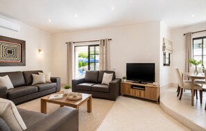 A modern living room with a sofa, a coffee table, a TV, and a dining area with chairs and a table.
