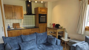 Un espace de vie compact comprenant un canapé bleu, des meubles en bois, un coin cuisine et une petite table avec une bouilloire.