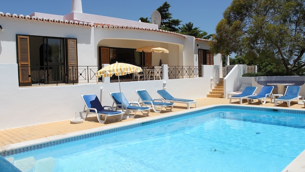 A swimming pool with lounge chairs and umbrellas, a white building with a tiled roof, and a clear blue sky. - Spacious luxury villa with A/C near beach with private pool (Carvoeiro)