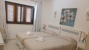 A bedroom with two beds, a window with blinds, a chair, a painting, and a lamp. - Spacious luxury villa with A/C near beach with private pool (Carvoeiro)