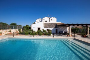 A pool area with a clear blue pool, a white building with a stone facade, and a pergola with outdoor seating. - Beautifully restored 16th Century farmhouse with large private pool  (Castellana Grotte)