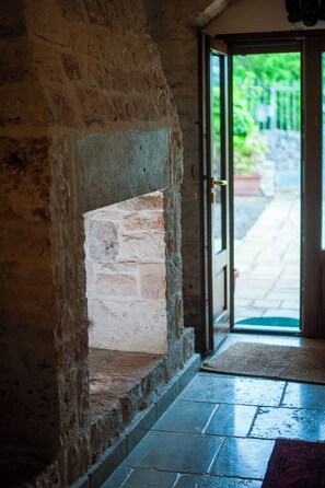 Une cheminée en pierre, une porte donnant sur l’extérieur et un sol carrelé.