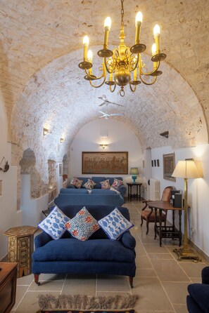 A room with a stone ceiling, a blue sofa with patterned cushions, a chandelier, and a framed painting on the wall. - Beautifully restored 16th Century farmhouse with large private pool  (Castellana Grotte)
