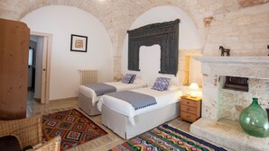 Une chambre avec deux lits, une cheminée, un vase vert et un tapis à motifs.