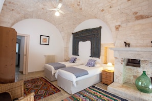 Un dormitorio con dos camas, una chimenea, un jarrón verde y una alfombra estampada.