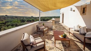 Une terrasse avec du mobilier d’extérieur, une table sur laquelle se trouve une pastèque, et une vue sur le paysage.