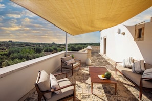Una terraza con mobiliario exterior, una mesa con sandía y vistas al paisaje.