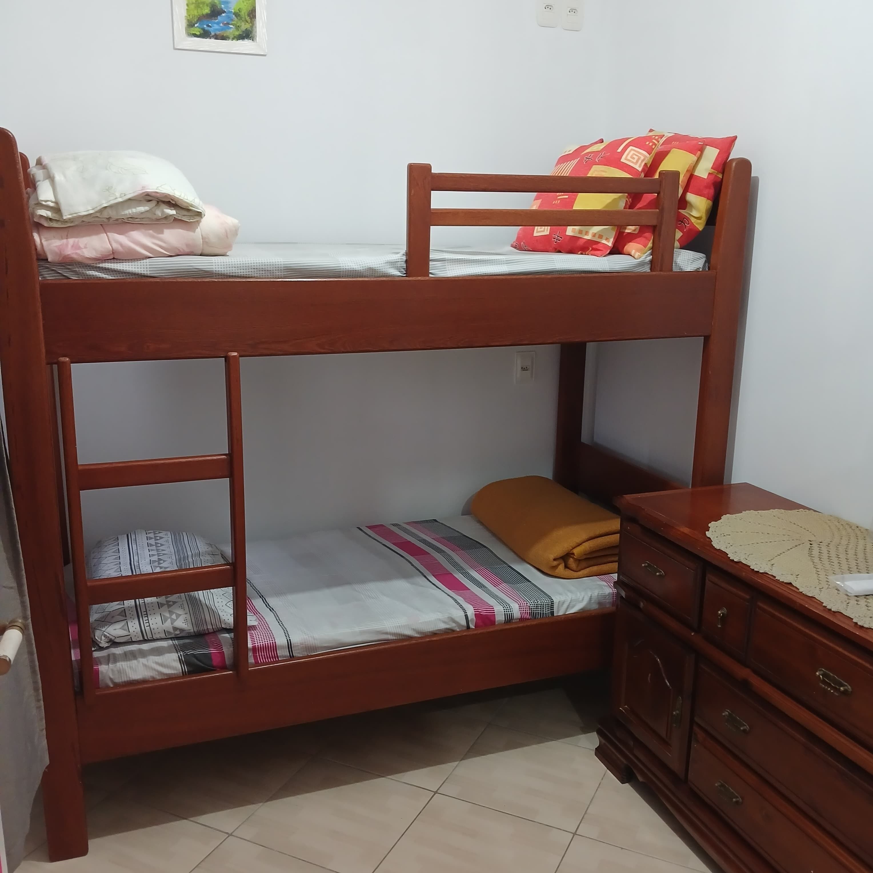 A bunk bed with a lower bunk, a wooden dresser, and a tiled floor.