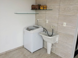 A compact laundry area with a washing machine and a sink, both white, in a room with tiled walls and floor. - Pousada Souza (Florianópolis)