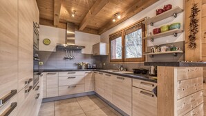 Eine moderne Küche mit Holzschränken, einer Edelstahl-Dunstabzugshaube und einem Fenster mit Jalousien.