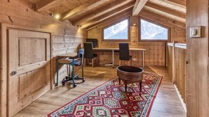 Eine Holzhütte mit hohen Decken, einem Schreibtisch mit Stühlen, einem großen Fenster und einem gemusterten Teppich.