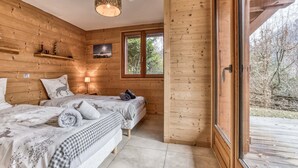 Ein Schlafzimmer einer Holzhütte mit zwei Betten, einem Fenster und Blick ins Freie.
