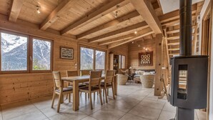 Ein Holzinnenraum mit Essbereich, Kamin und großen Fenstern mit Blick auf Berge.