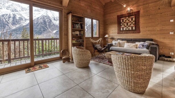 Ein gemütliches Holzhaus mit Balkon, Bücherregal, Sofa und Korbmöbeln.
