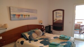 Une chambre à coucher comprenant un lit, une table de chevet, une lampe, une chaise, une table à manger et un tableau accroché au mur.
