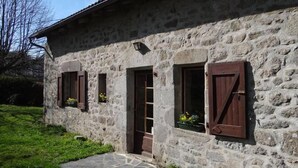 A stone building with wooden shutters, a small entrance, and a stone pathway leading to the door.