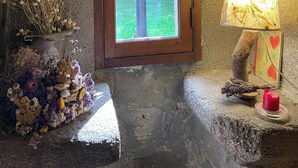 A rustic room with a wooden door leading to a garden, a lamp, and a vase with dried flowers.