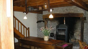 A rustic dining area with a wooden table, bench, and hanging light fixtures. A stone fireplace is visible in the background.