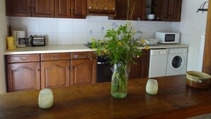 A kitchen with wooden cabinets, a microwave, a washing machine, and a vase with flowers on the counter.