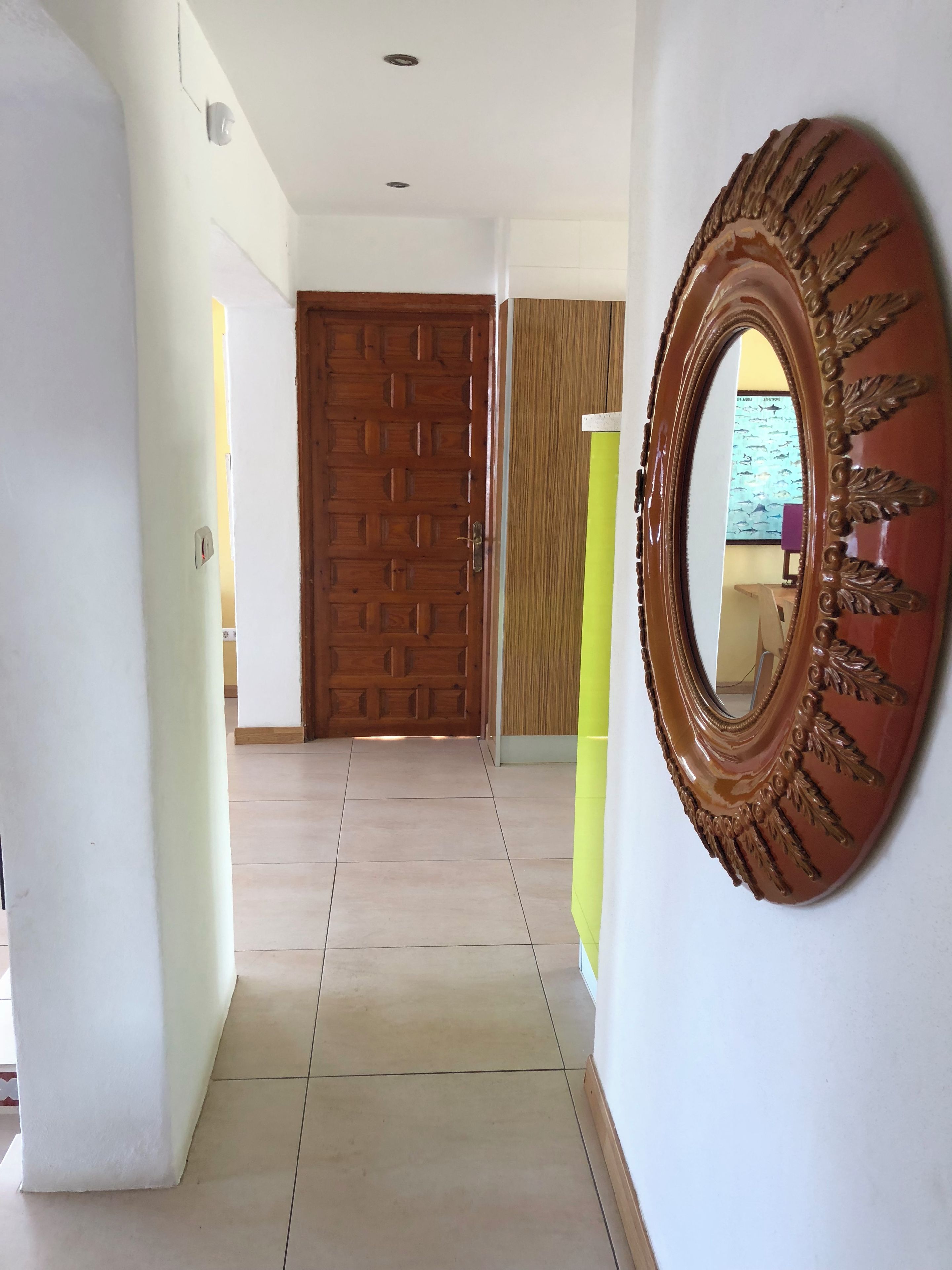 Un pasillo con una puerta de madera, un espejo y suelo de baldosas.