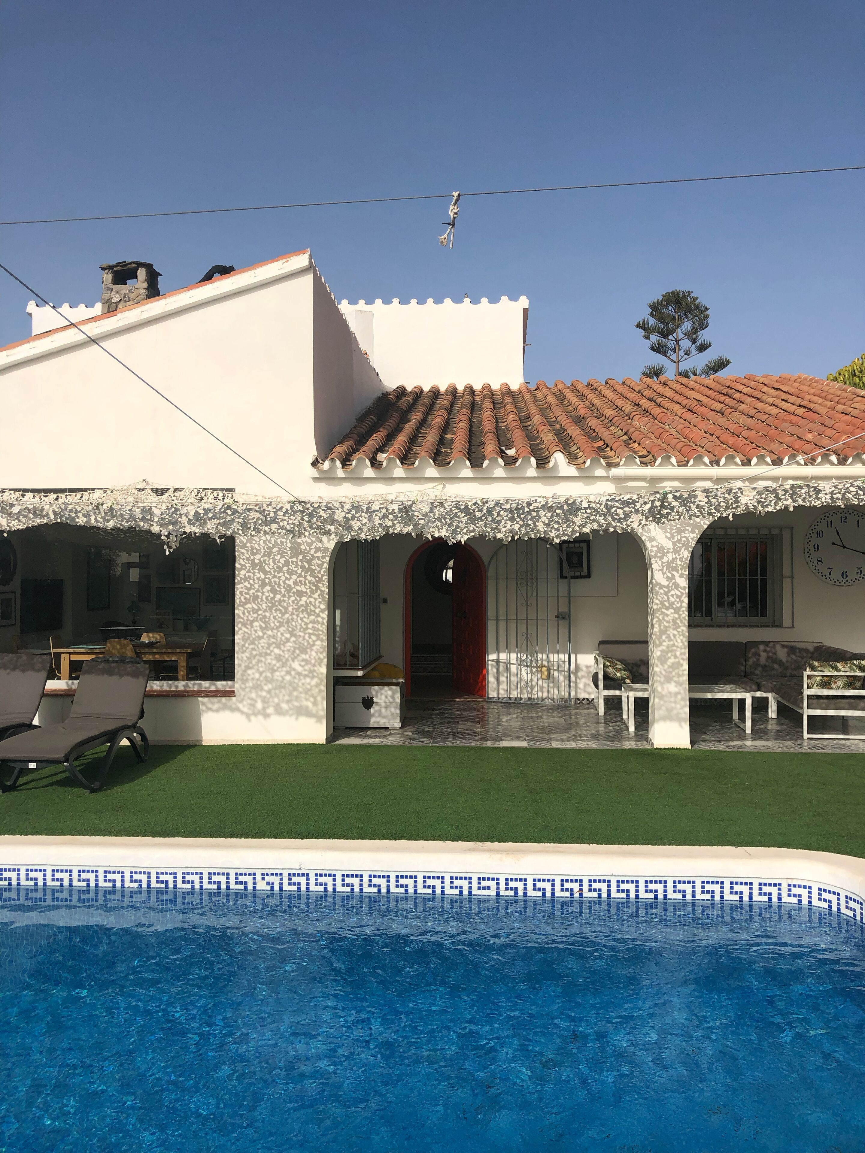 Una casa con piscina, techo de tejas y un patio cubierto.