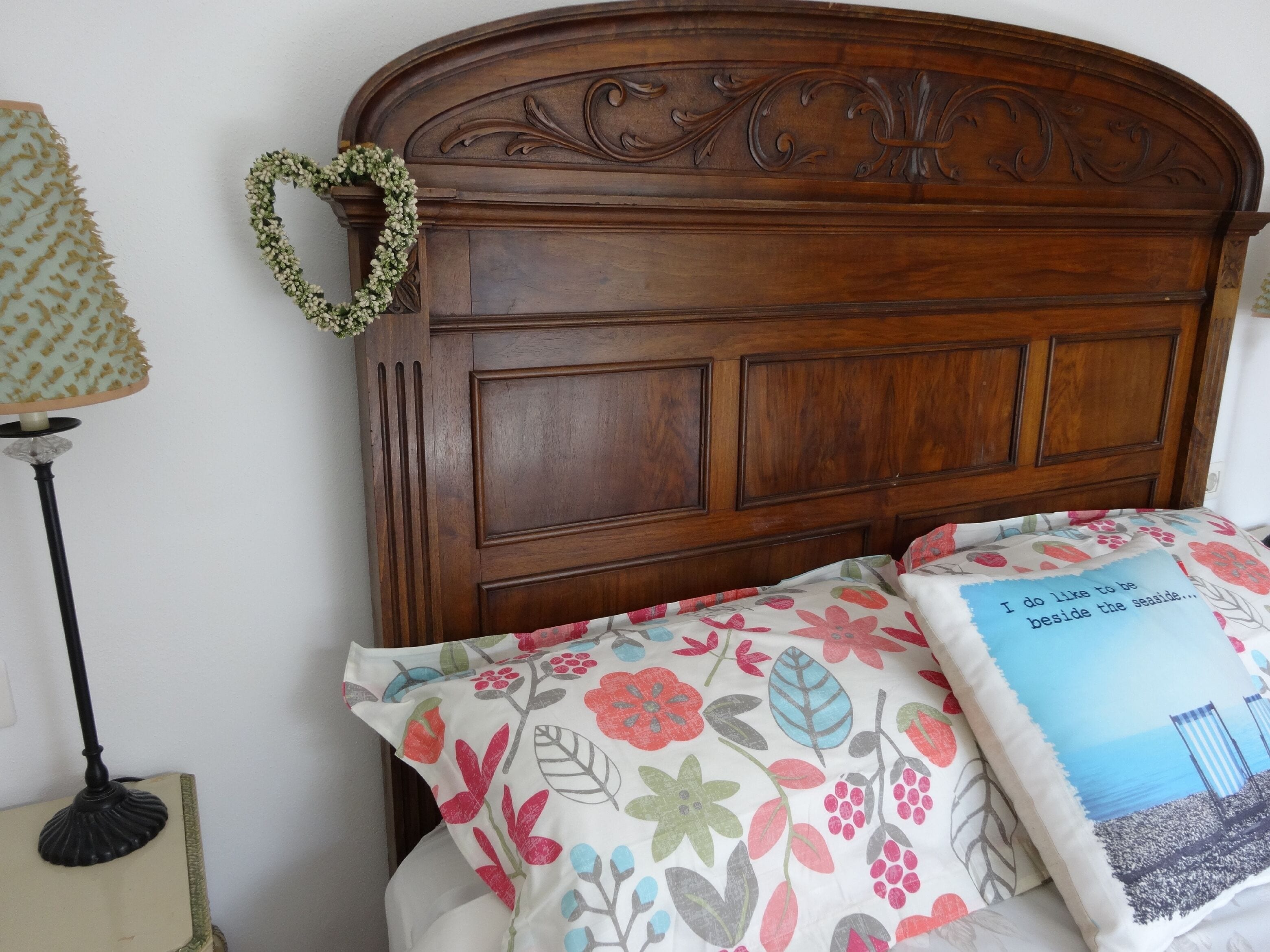 A wooden headboard with floral bedspread and a pillow with a beach scene.