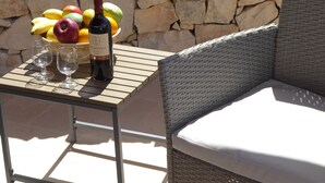 A wicker chair with a cushion, a table with a bottle of wine and glasses, and a bowl of fruit. - Beautifully Restored Trullo In Idyllic Location (Cisternino)