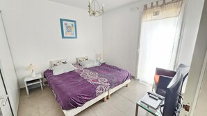 A bedroom with a large bed, two bedside tables, a desk with a chair, a chandelier, and a window with curtains. - Luxury mini villa with garden & swimming pool in residence, 800m from the beach (Zonza)