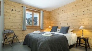 Habitación con paneles de madera, una cama, dos lámparas de noche, una silla y una ventana con cortinas.