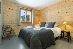 Um quarto com painéis de madeira, uma cama, duas luminárias de apoio, uma cadeira e uma janela com cortinas.