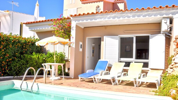 A pool area with a clear pool, a table with an umbrella, and several lounge chairs.